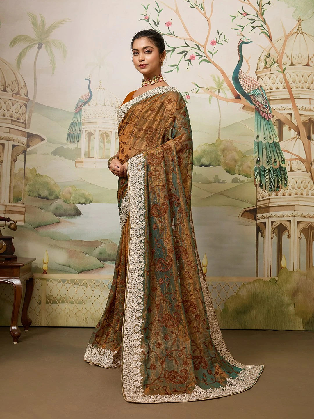 Woman in a traditional saree with a decorative background featuring peacocks and architectural elements.